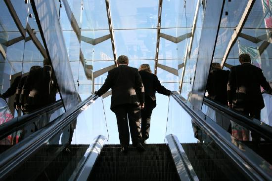 Two business people walk up an escalator.