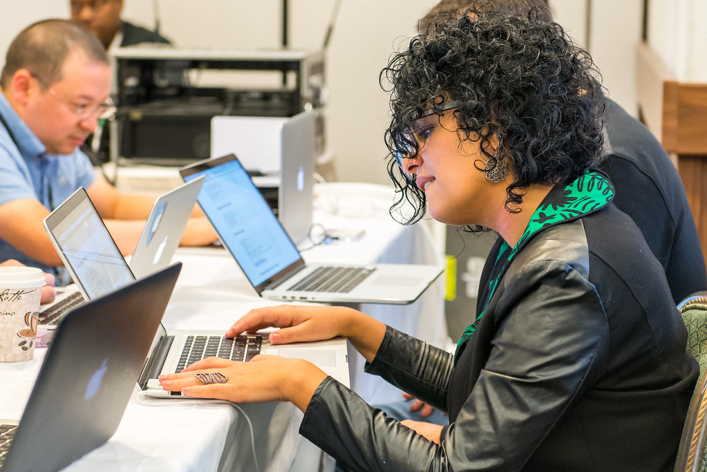 Woman on laptop with a man on a laptop in the background