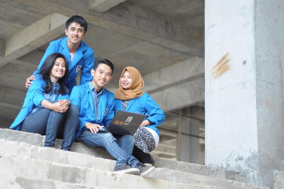 A group of 4 diverse students pose for a picture all dressed in blue.