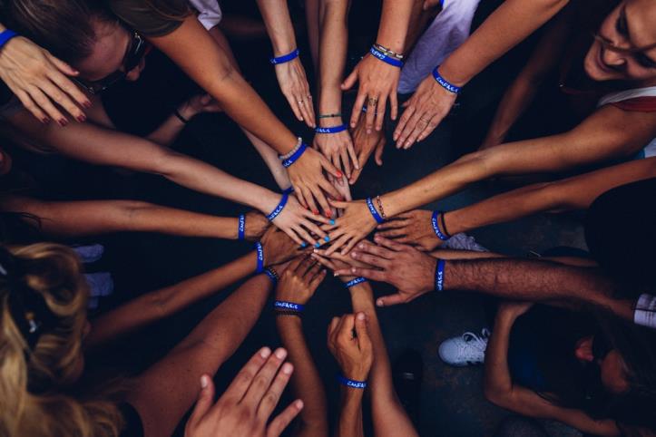 A diverse group of people all placing their hands on top of one another in a group.