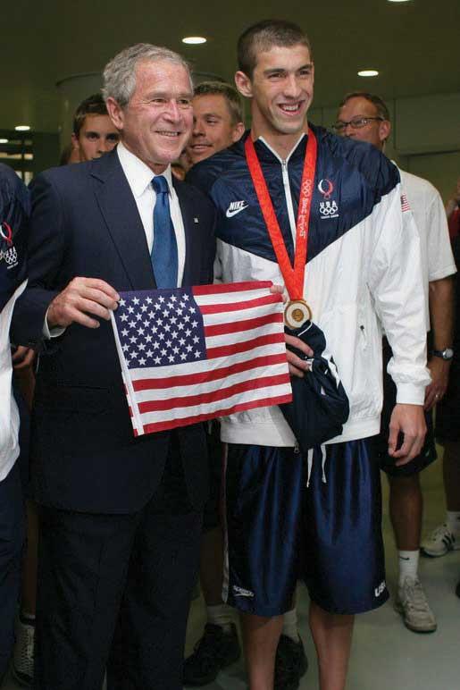 Michael Phelps standing with George Bush as he holds an American flag