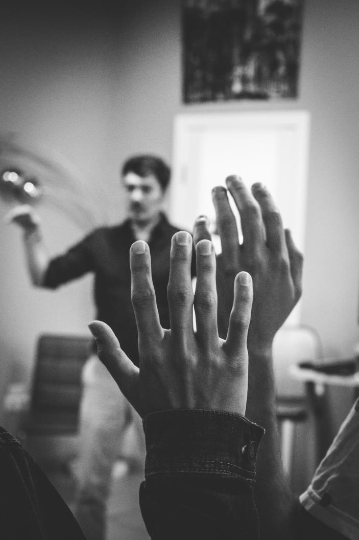 A student raises their hand in class, with their instructor in the background.