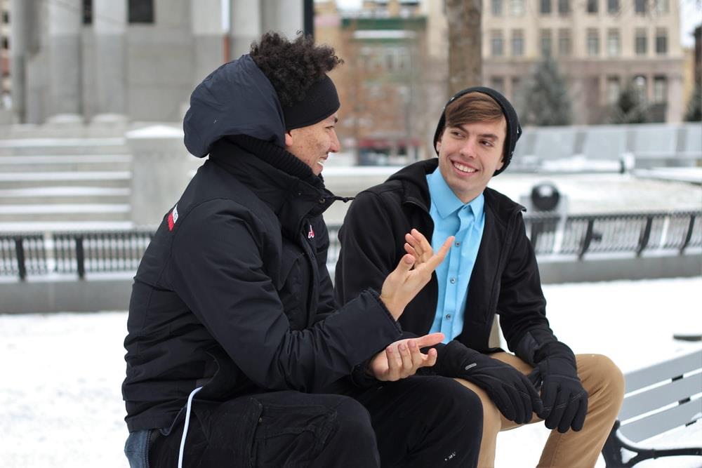 Two men talk to each other while seated at a bench.