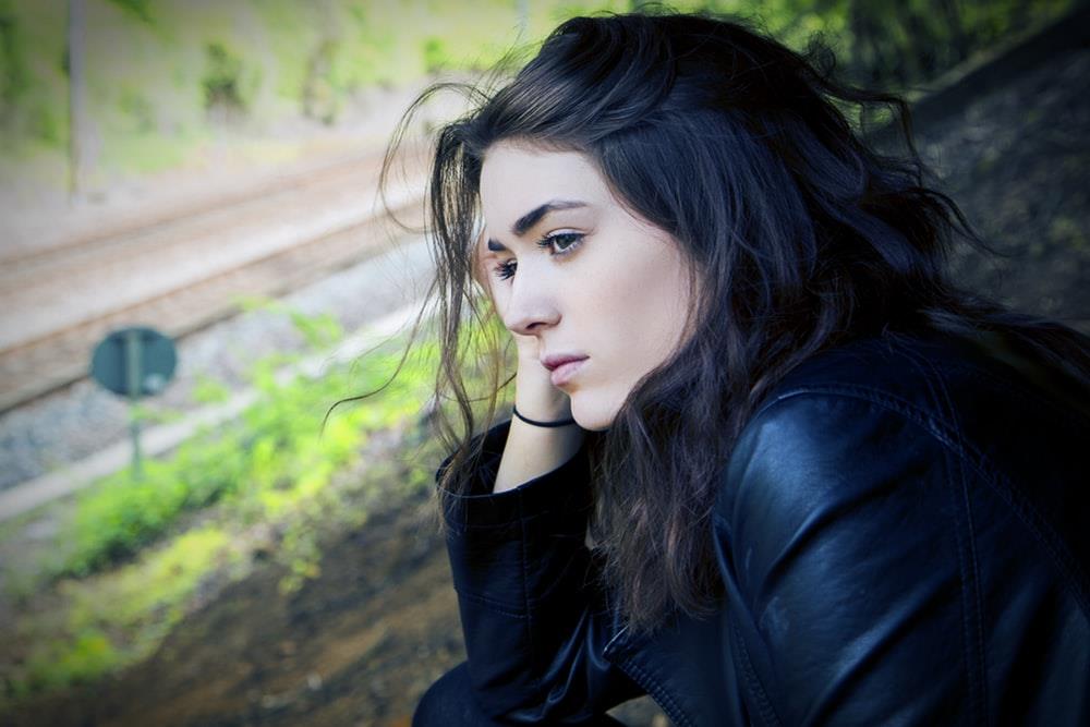 A woman contemplates on a hill near a train track.