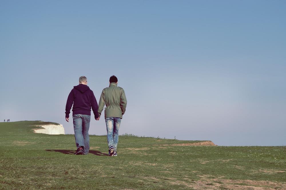 A couple holds hands while they walk on the coast.