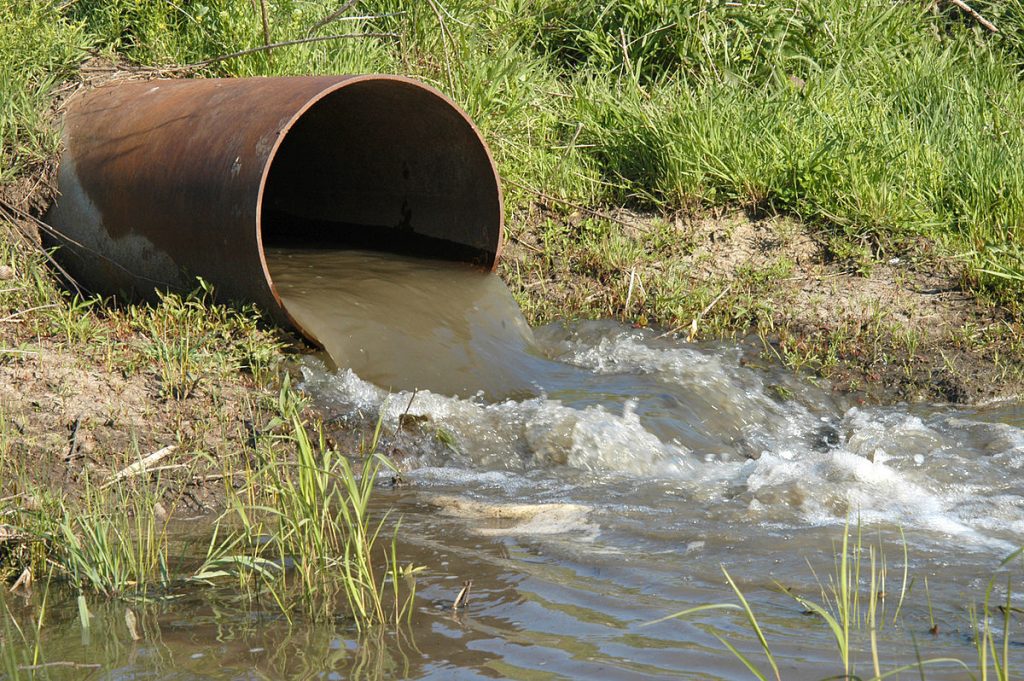 Photo shows large pipe discharging brown water into a body of water.