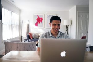 A person sits at a desk and smiles while looking at their open Macbook laptop