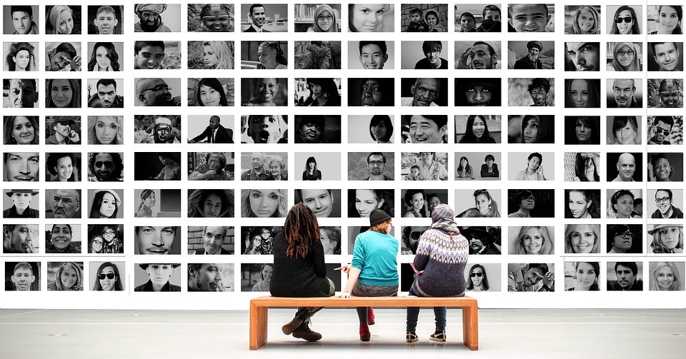 Three people sitting on a bench looking at a wall of photos