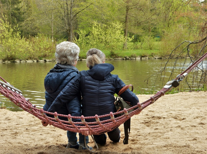 two people facing lake sitting on a hammock