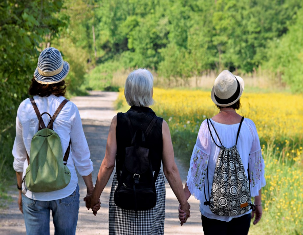 3 people facing backwards holding hands walking on an outdoor path