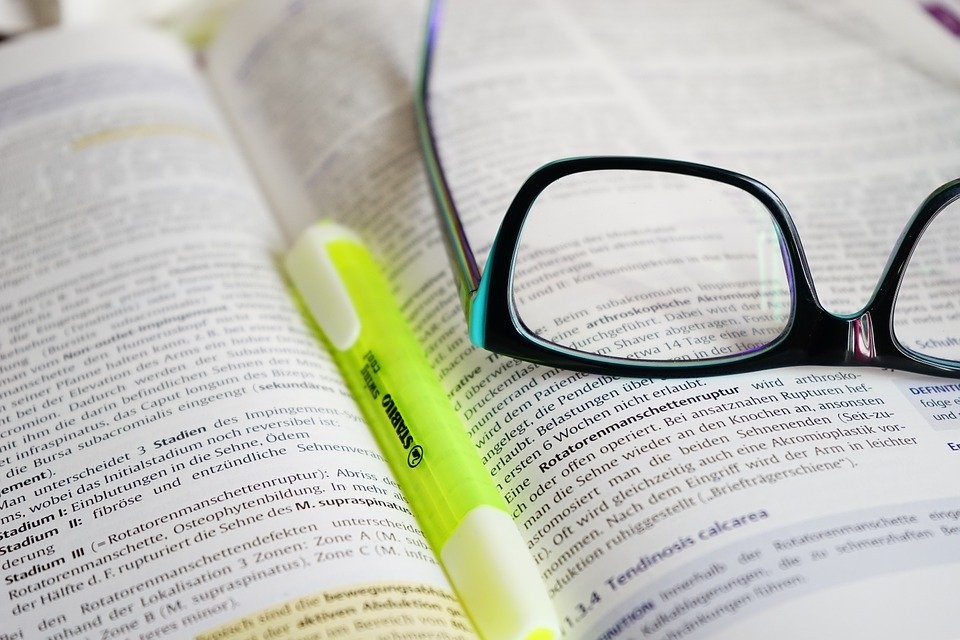 reading glasses and highlighter marker on top of a book