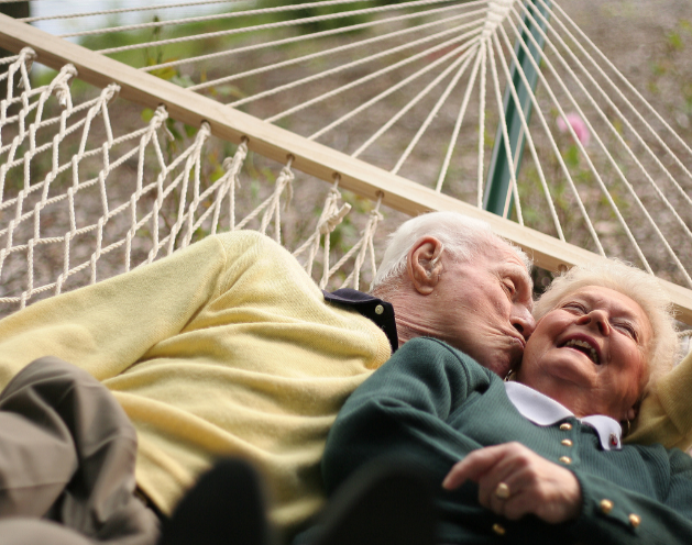 two older adults on a hammock with one kissing other on cheek while other is smiling