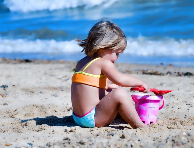 toddler on the beach playing with sand bucket and shovel