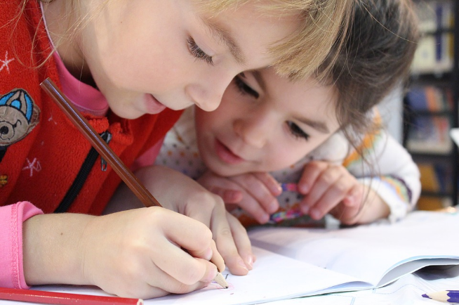 child writing and another looking overs shoulder