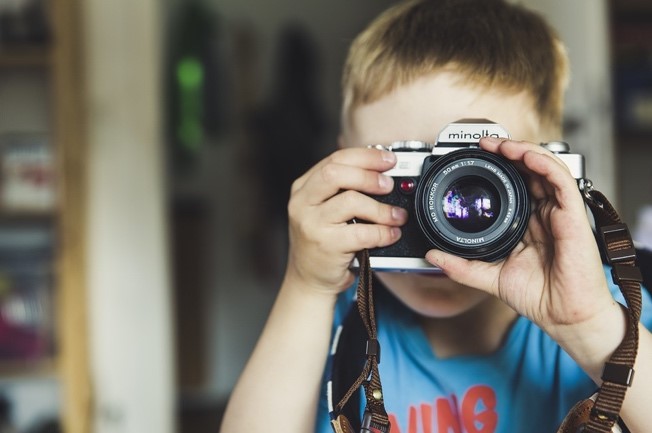 Young child taking a picture with a camera and looking through the lens.