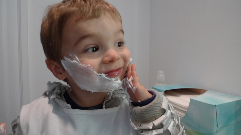 Young boy is putting shaving cream on his face in a bathroom.