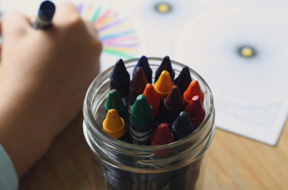 young hand coloring next to a jar of crayons