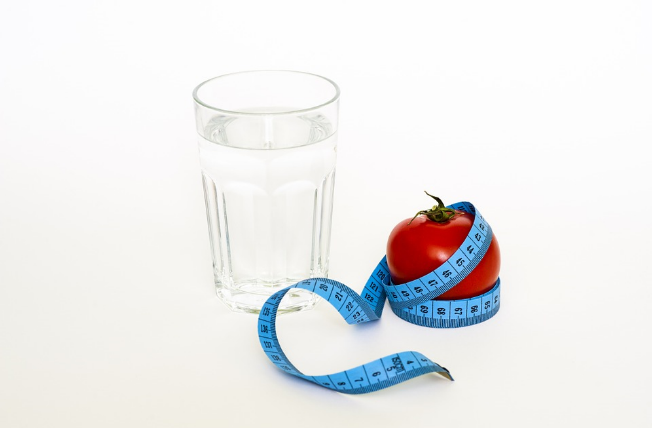 Glass of water on left and tomato wrapped around measuring tape on right