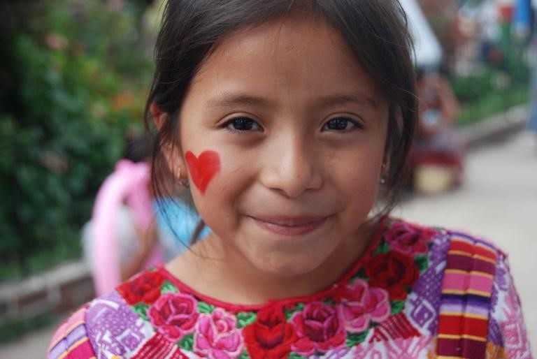 child with closed mouth smile and heart painted on cheek