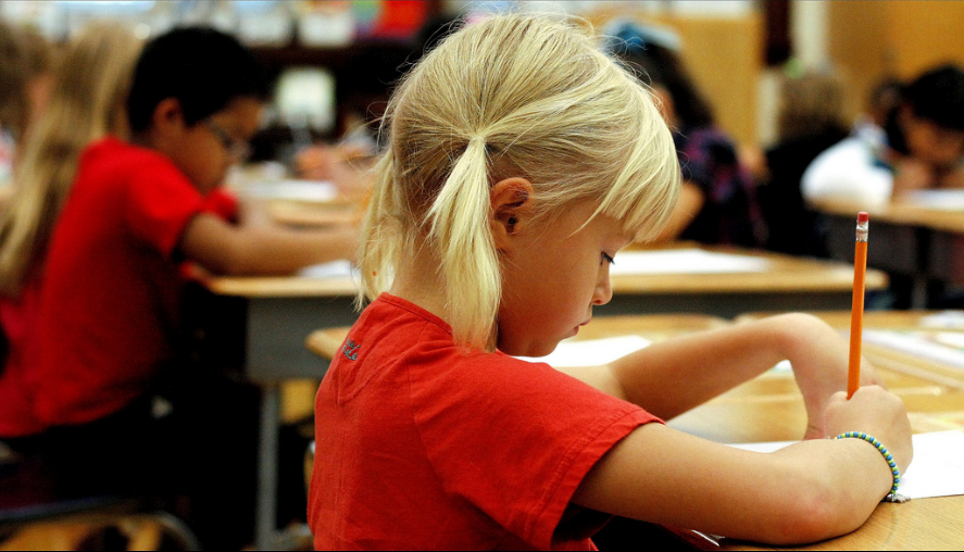 students at desks writing with red shirts on