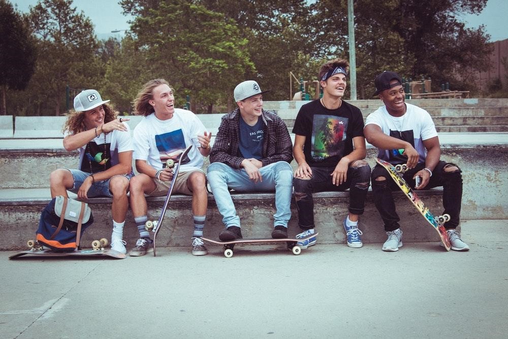 5 teens with skateboards sitting and laughing