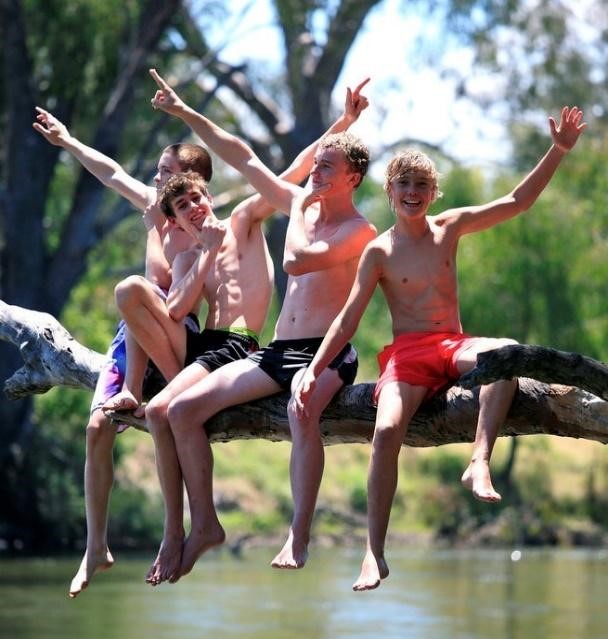 4 kids sitting on a tree branch over water wearing swim trunks