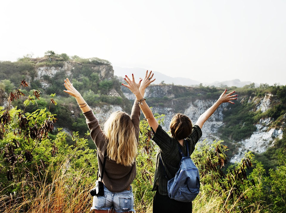 two people facing backwards with hands up looking at mountain view