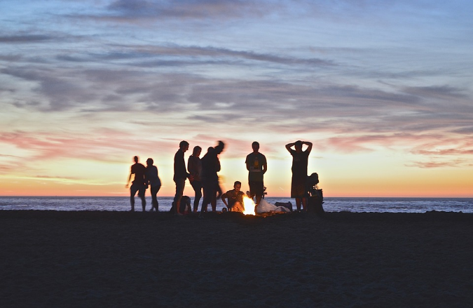 large group of people at the beach at sunset with a campfire