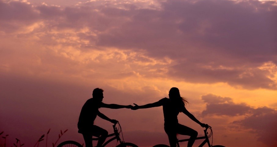 two people on bikes during sunset reaching out for each other's hands