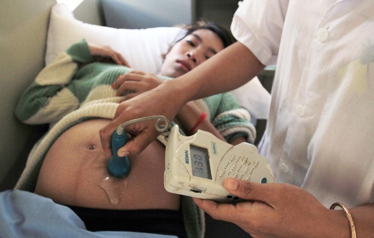 Medial staff checking heartbeat of fetus using doppler on pregnant woman's belly