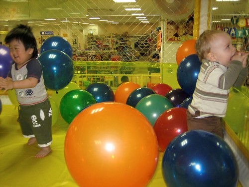 two toddlers with large balloons around them on the ground