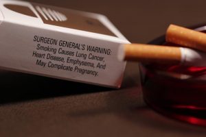 A photograph shows a cigarette, an ashtray, and a surgeon's general warning.