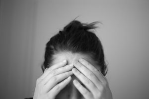 A photograph of a woman holding her forehead in pain
