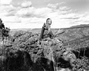 Photo of a man sitting on a mountaintop with a bow and arrow