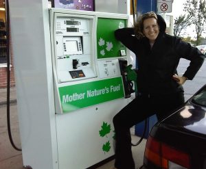 Woman standing next to a gas pump labeled Mother Nature's Fuel