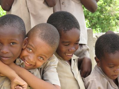 A row of young black male children are smiling and laughing; their arms are around one another.