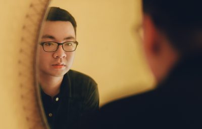 Young adult Asian man is staring at his reflection in a mirror.