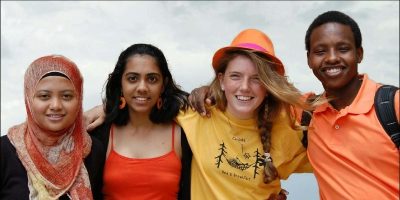 Four college students from different nationalities have their arms around one another's shoulders, they are smiling.