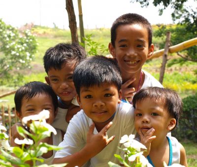 Five Filipino boys are grouped together smiling. They are in a forested area.