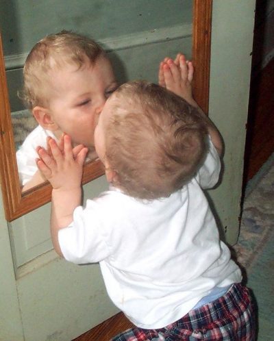 Small toddler is kissing their reflection in a mirror.