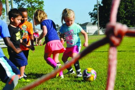 Two school aged female children are kicking a soccer ball in a playground.