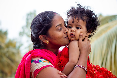 An Indian mother in a red sari is kissing her toddler. 