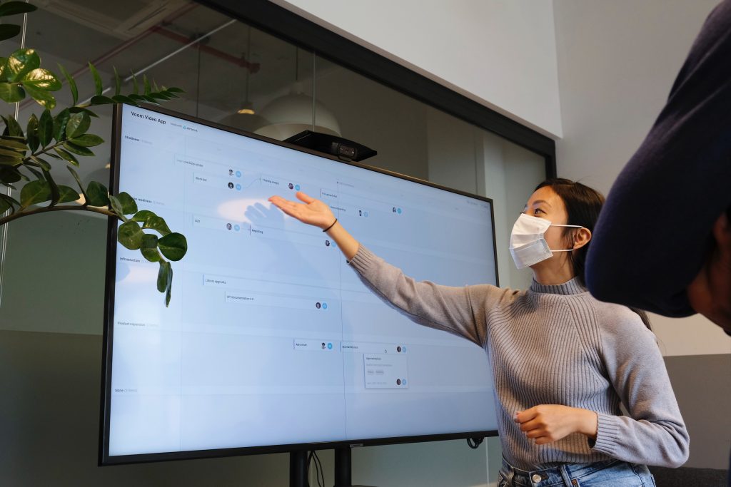 Woman presenting at TV display wearing a mask