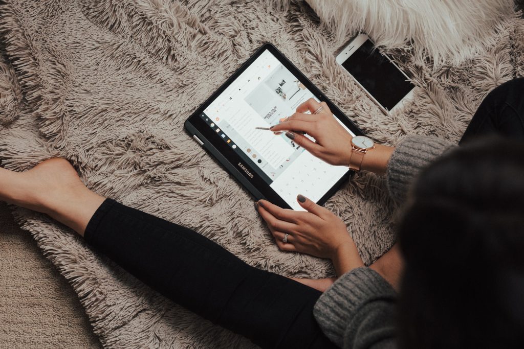 close-up of woman sitting on bed alone using a tablet computer, iPhone next to her