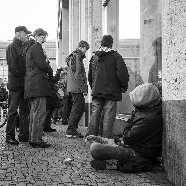 People wearing Jackets and standing or sitting on the sidewalk