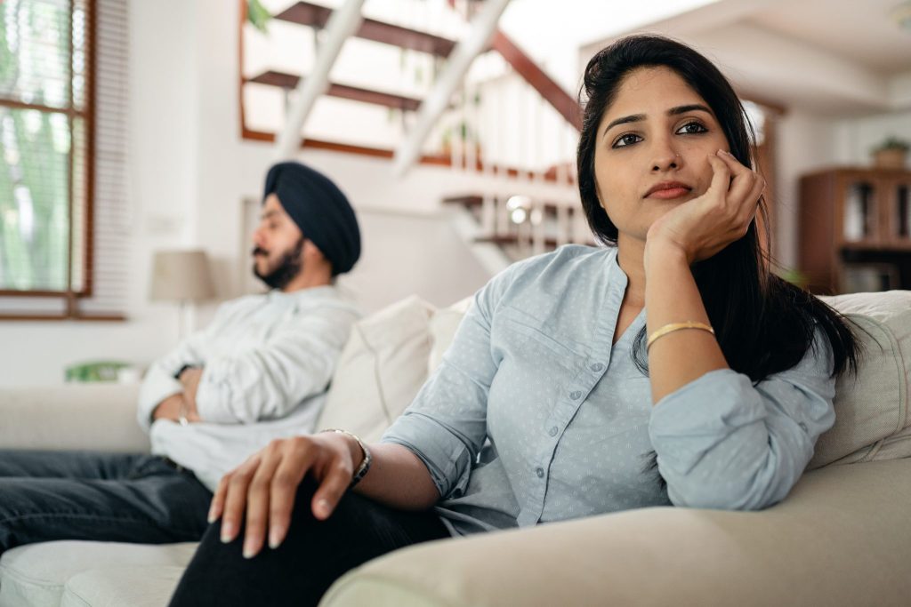 A man and woman sit on a couch, face away from one another