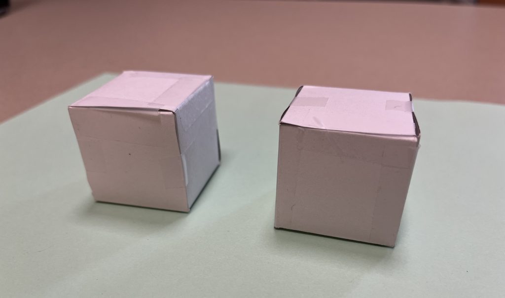 Two small boxes constructed from grey card stock sit side-by-side on a table