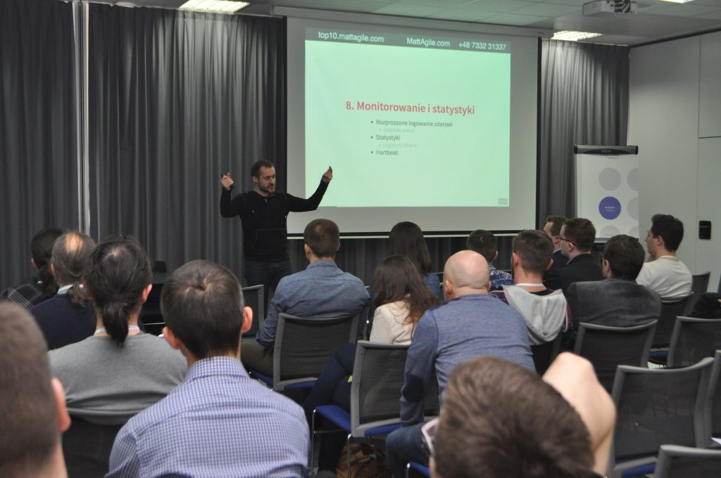 A man speaking and presenting a powerpoint in front of a group of seated people.