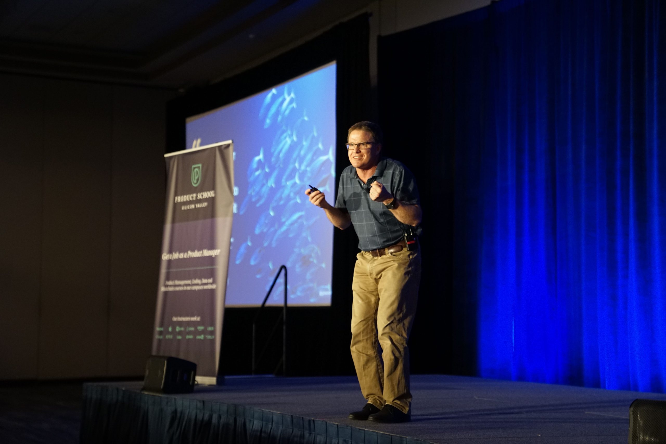 A man standing on a stage giving a presentation while holding a slide clicker remote to control the slides