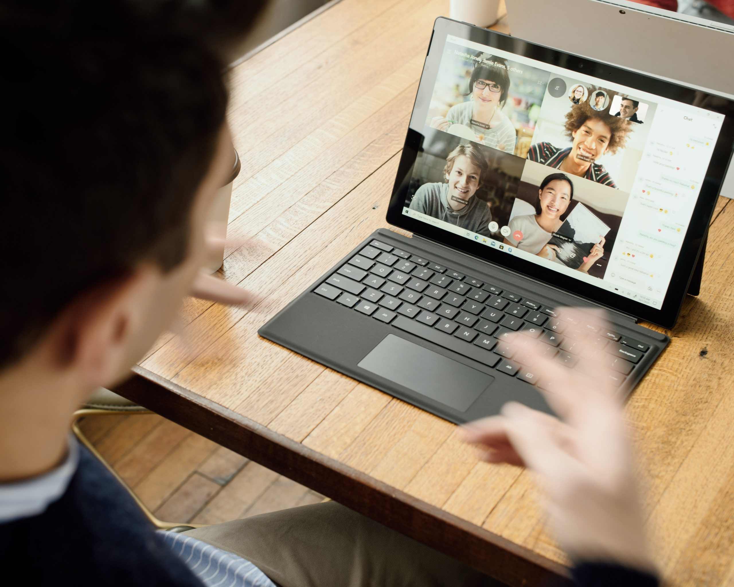 A man sitting in front of a virtual meeting with four other people on the laptop screen.